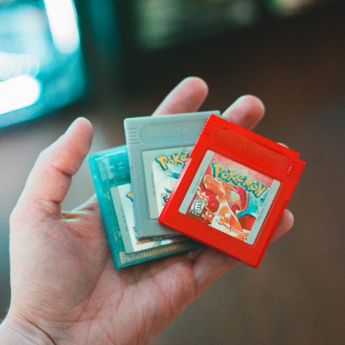person holding red and green nintendo game cartridge